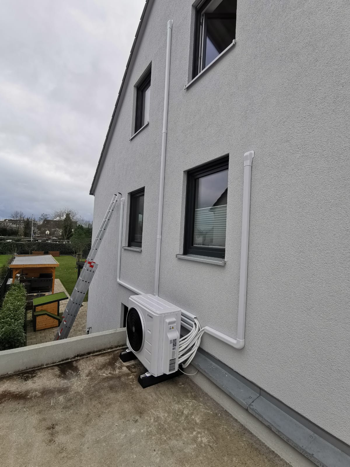 Außengerät einer Klimaanlage ist an der Hausfassade montiert, mit sauber verlegten Leitungskanälen bis in die oberen Etagen.